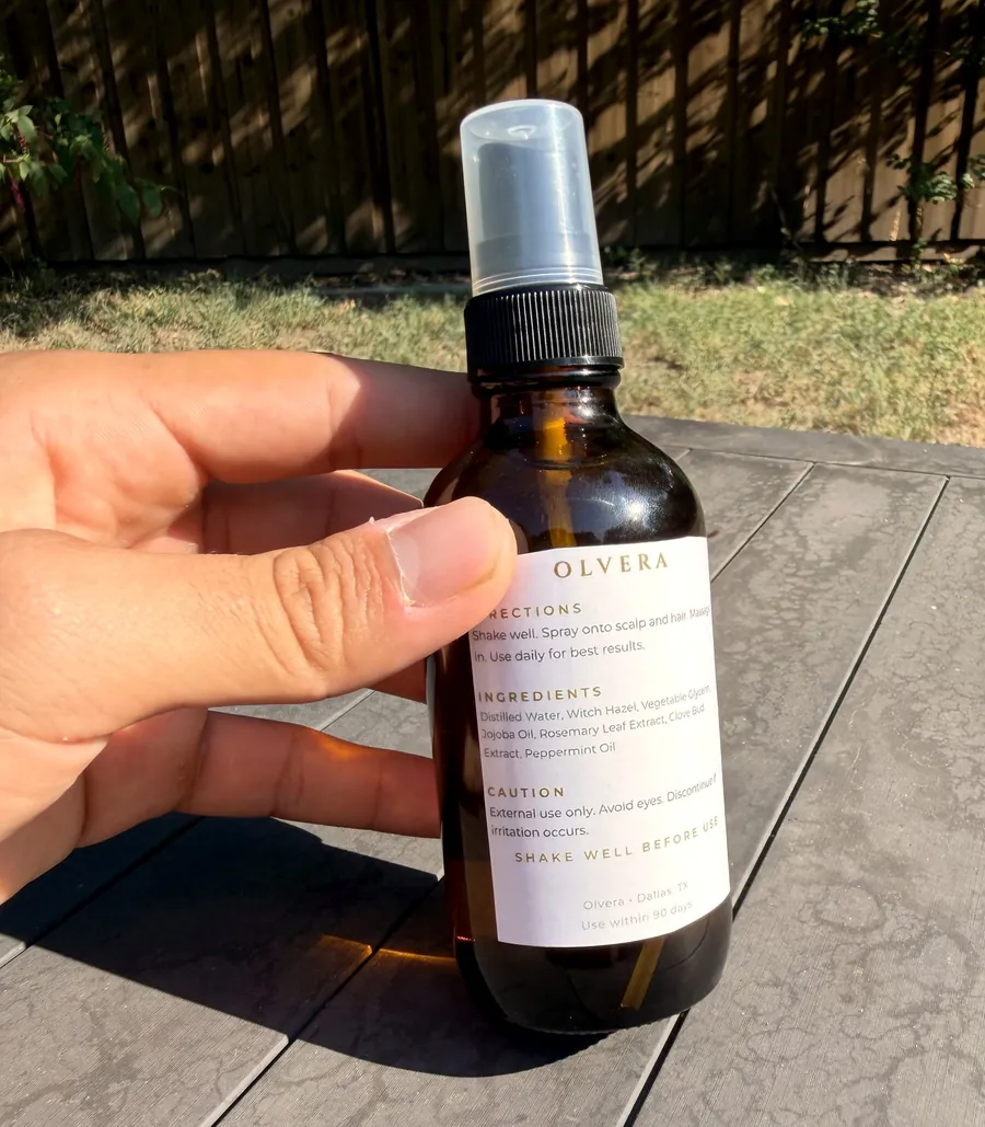 A bottle of OLVERA Hair Elixir held in one hand
